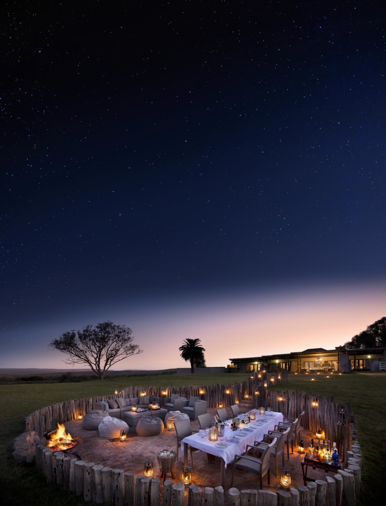 An outdoor dining setup with a long table surrounded by lights under a starry night sky.