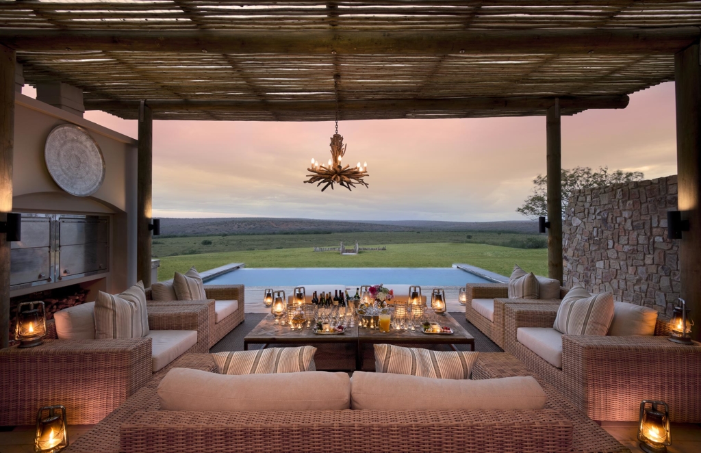 A stylish outdoor lounge area with wicker seating and a view of a scenic landscape at sunset.