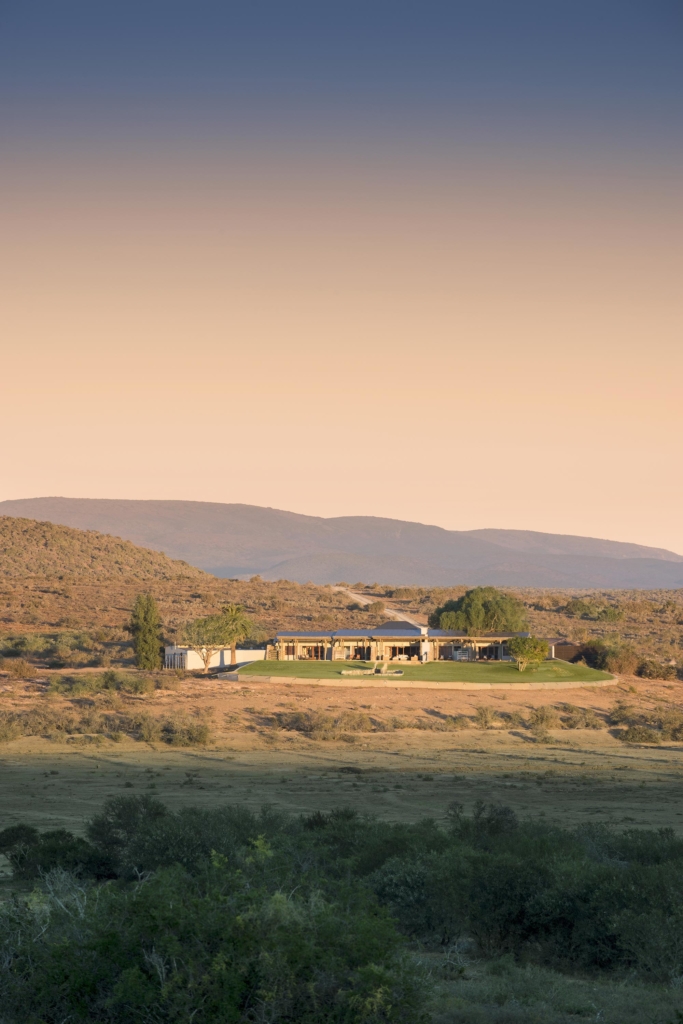 A modern house is situated in a rural landscape with mountains in the background.