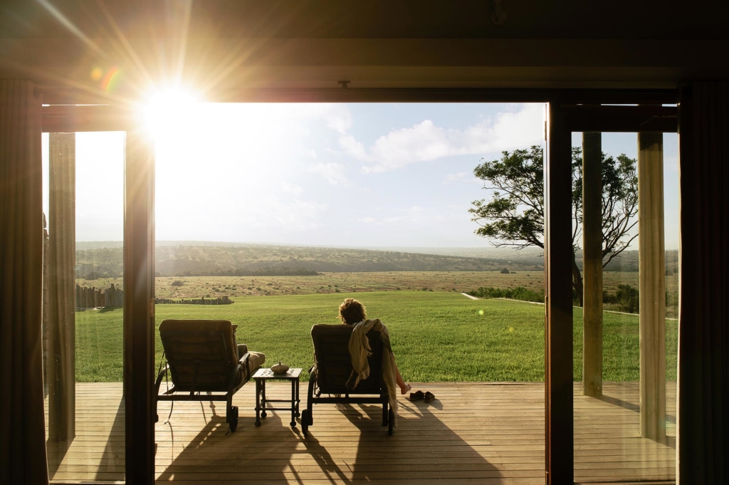 Two people relax in chairs on a deck overlooking a vast landscape at sunset.