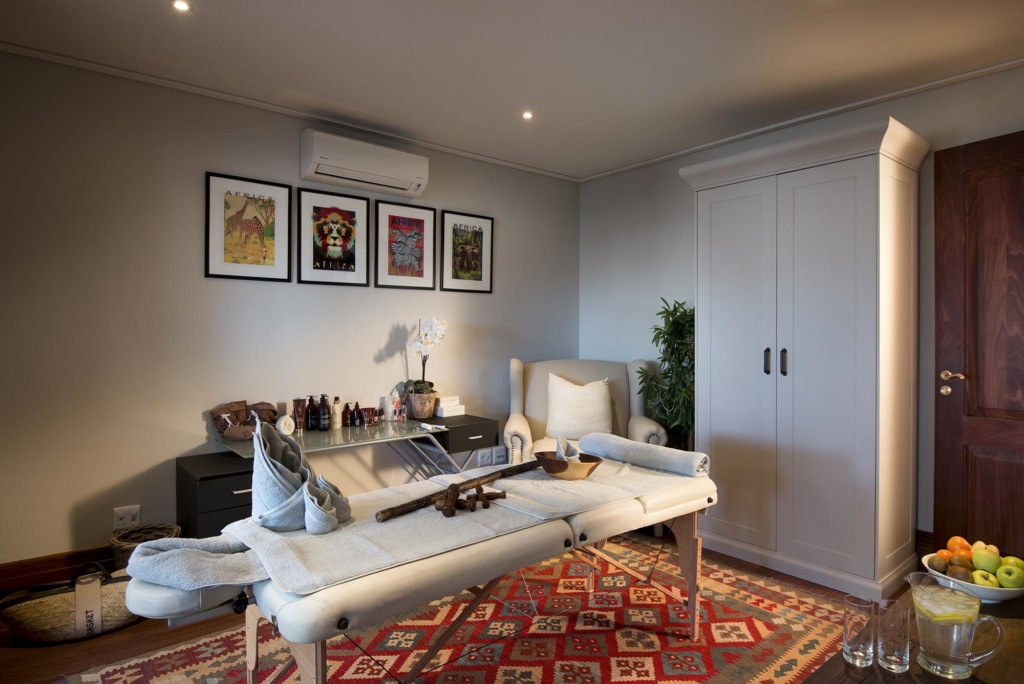A serene treatment room featuring a massage table, artwork on the walls, and a wardrobe.