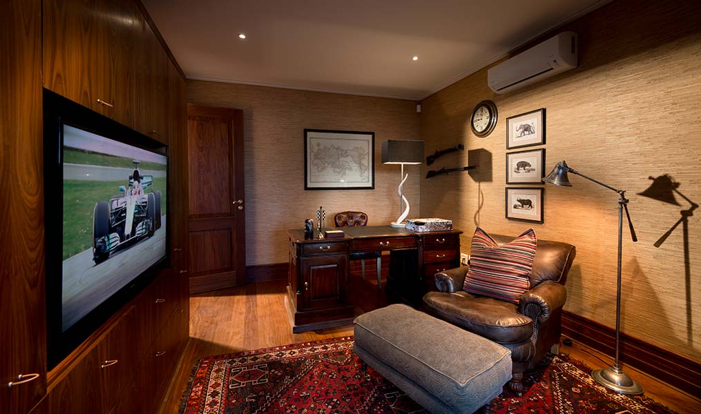 A stylish office featuring a desk, comfortable chair, wall-mounted television, and decorative artwork.