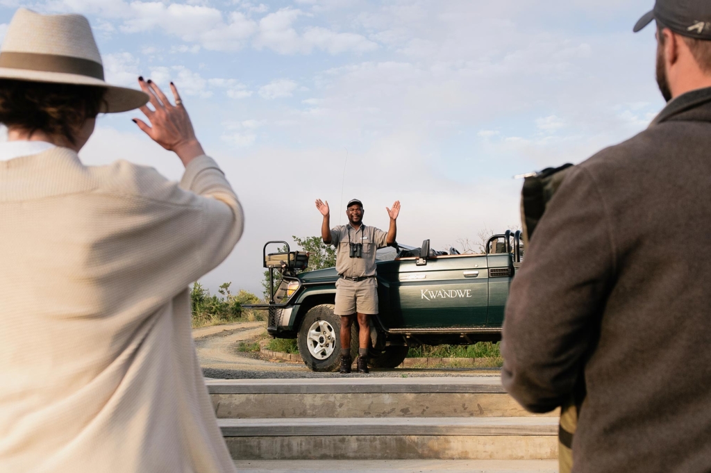 A person gestures from a vehicle while two others watch nearby.