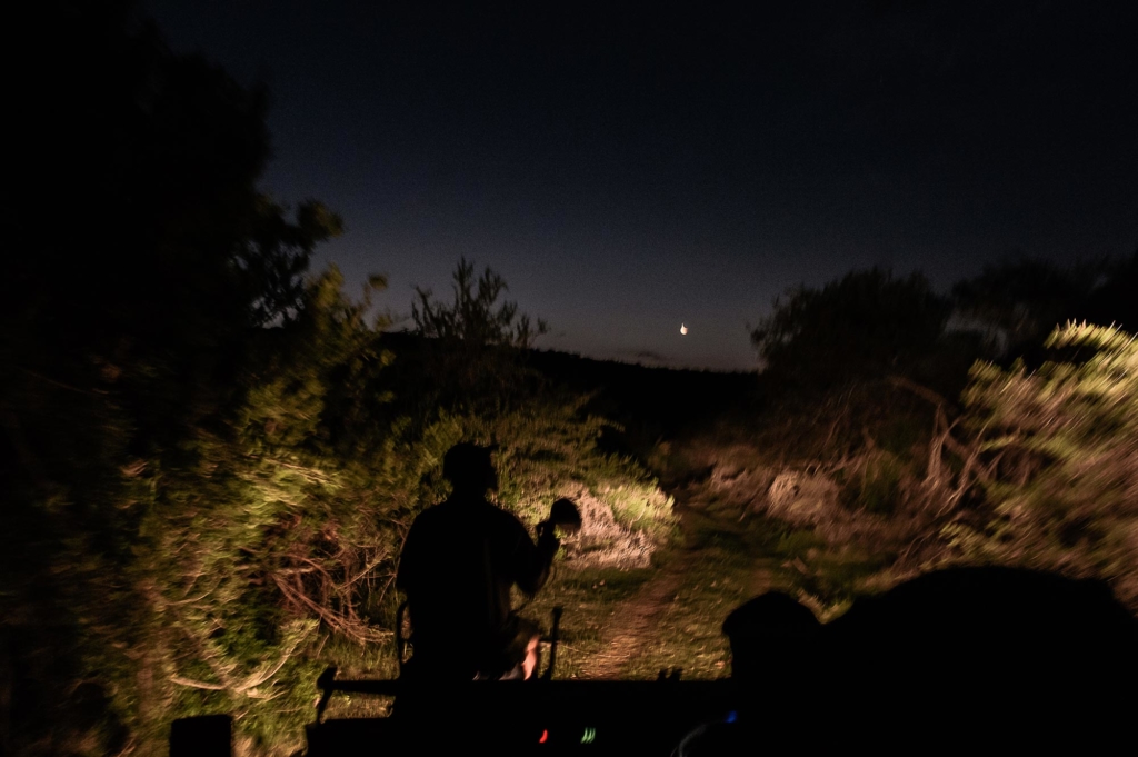 Silhouette of a person on a vehicle in a dark, natural landscape with a light in the background.