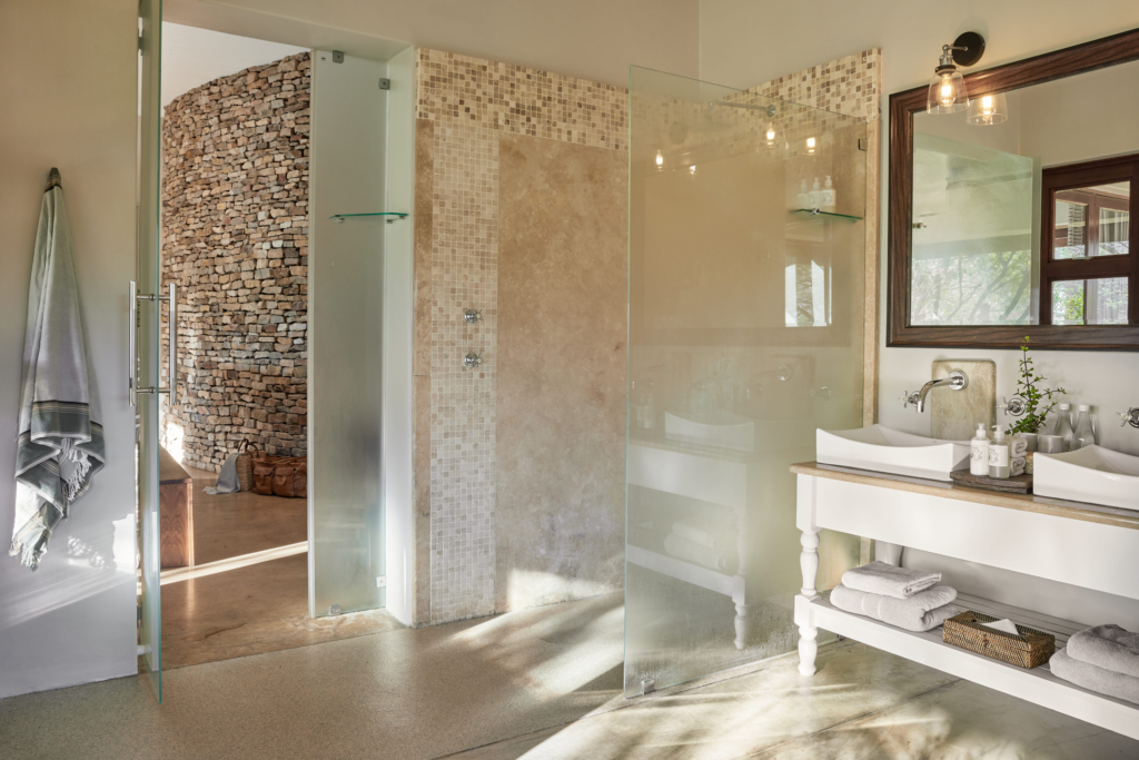 Modern bathroom featuring a double sink, glass shower enclosures, and stone accent wall.
