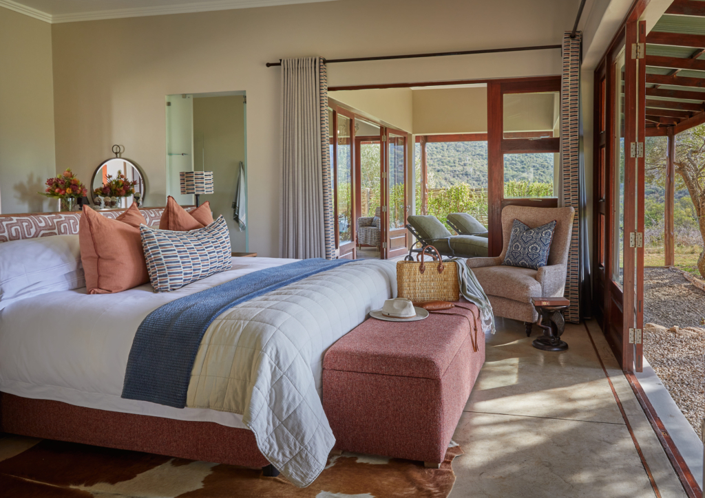 A cozy bedroom featuring a bed with decorative pillows, a chair, and large windows overlooking a natural landscape.