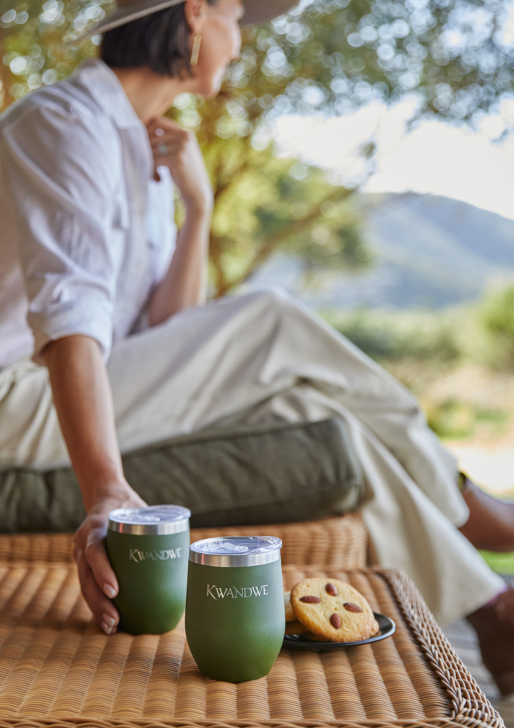 A person seated outdoors holds two green cups next to a plate of cookies.