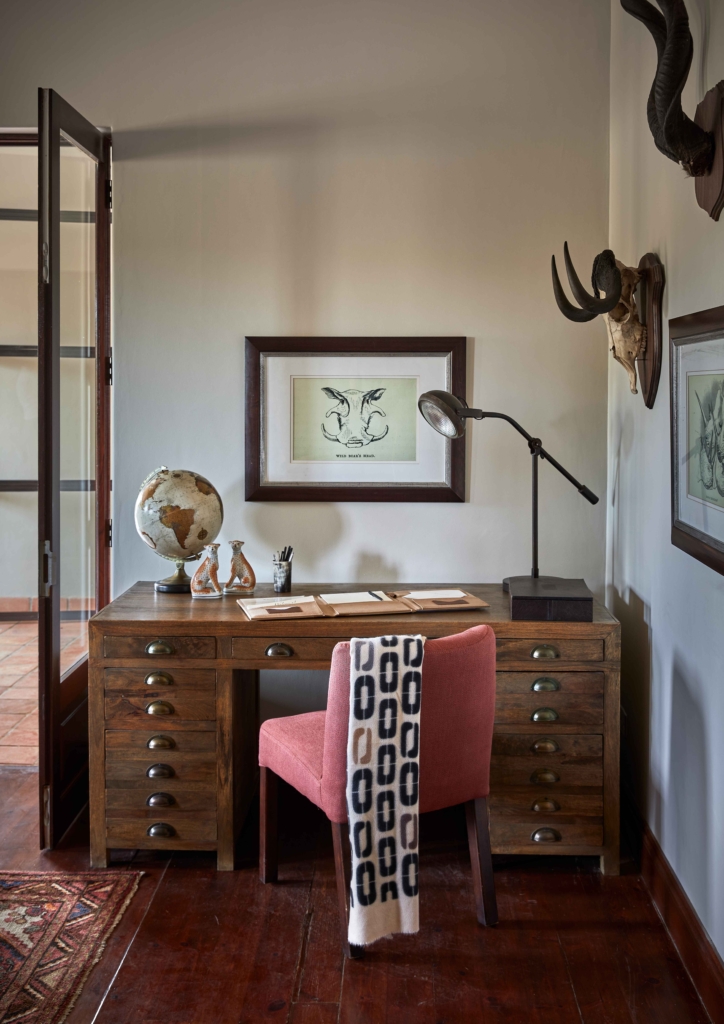 A stylish home office featuring a wooden desk, pink chair, globe, and framed artwork.
