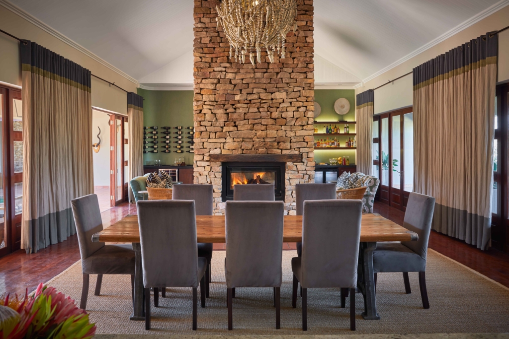 A modern dining room featuring a large wooden table, upholstered chairs, and a stone fireplace.