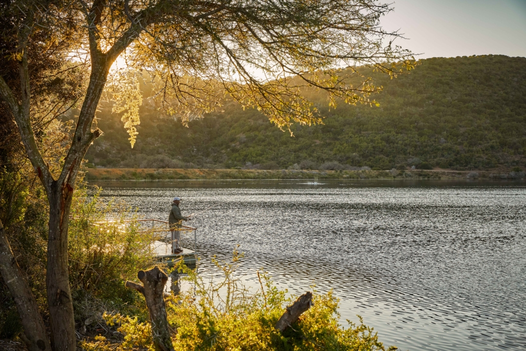 A person fishing from a dock by a tranquil lake at sunset.