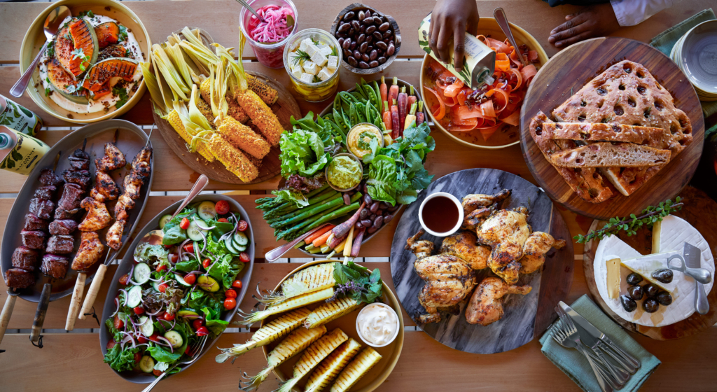 A spread of various food dishes including grilled meats, salads, and vegetables on a table.