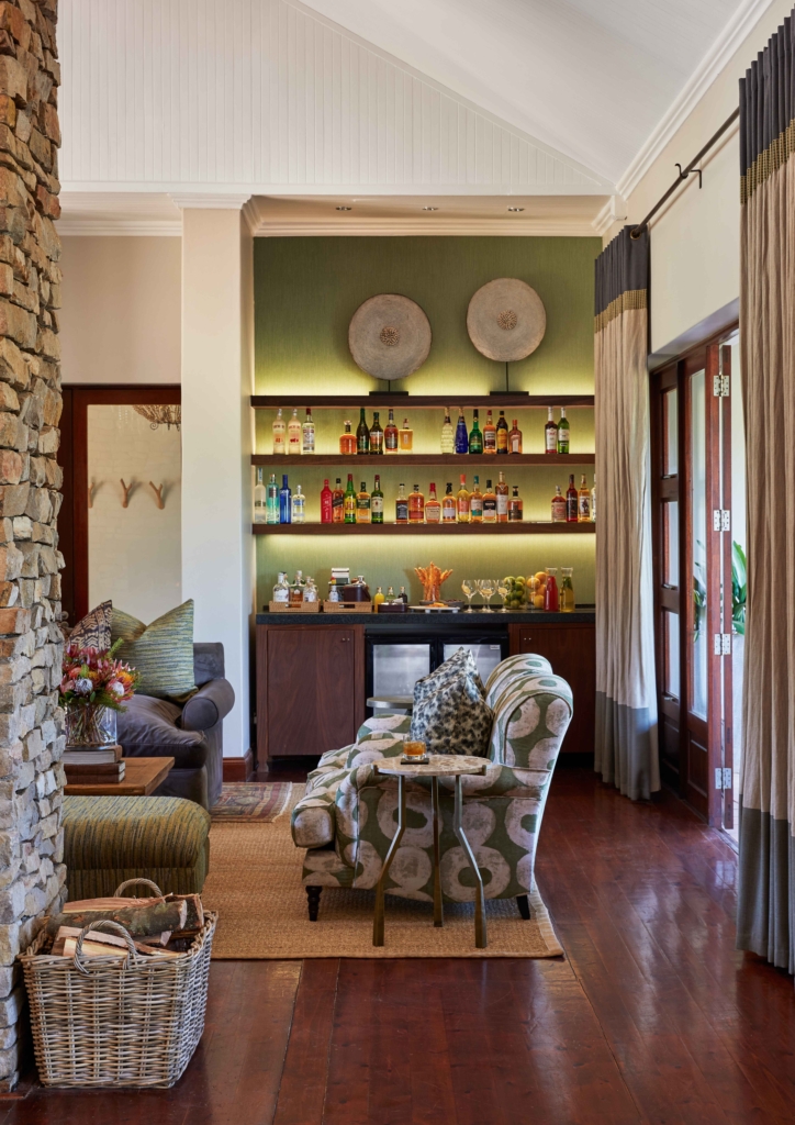 A cozy living room with a stone wall, bar shelf displaying colorful bottles, and comfortable seating.