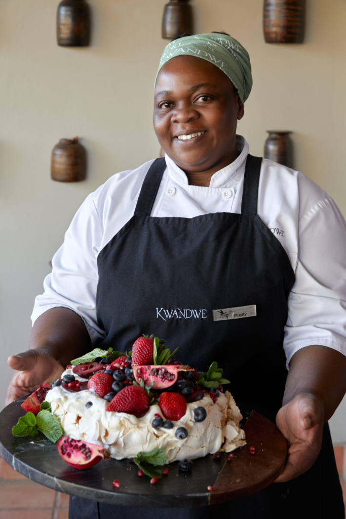 A chef holding a decorated pavlova dessert surrounded by fresh fruit.