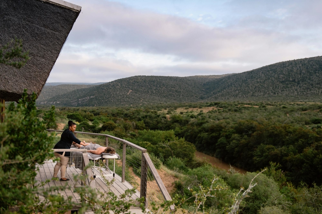 A person receiving a massage on a terrace overlooking a lush landscape.
