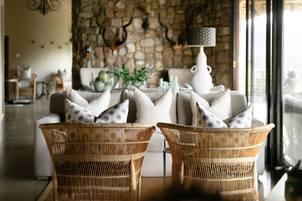 A cozy living room featuring wicker chairs, decorative pillows, and a stone wall.