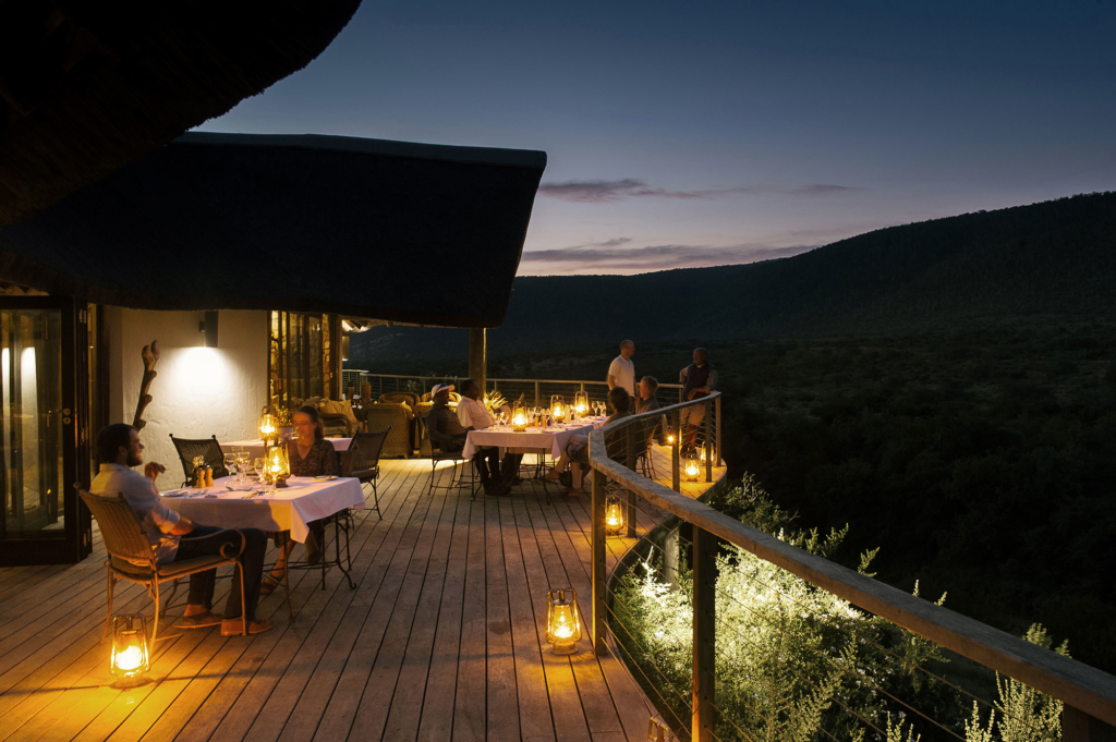 A dining area with candlelit tables on a wooden deck overlooking a sunset landscape.