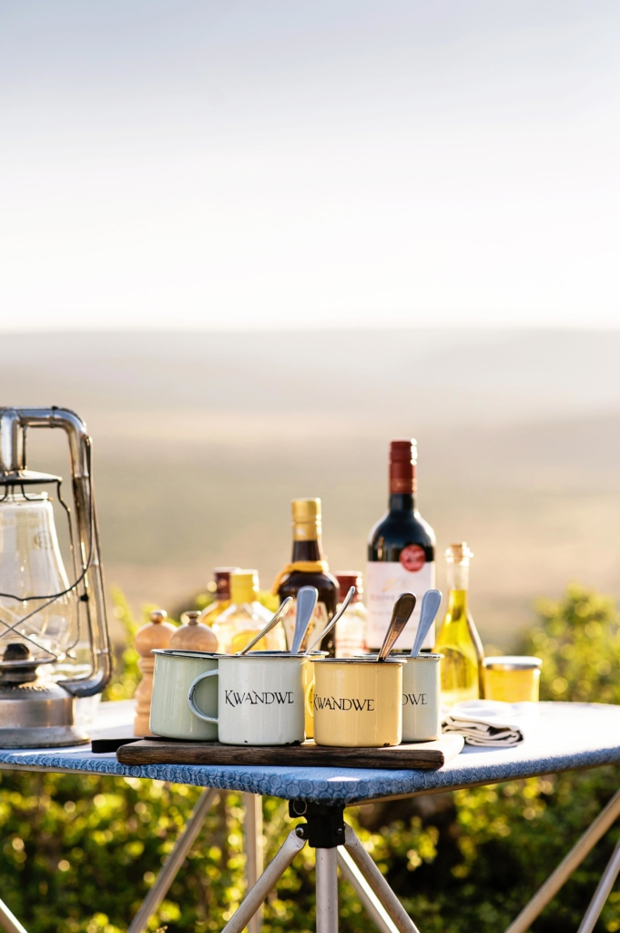 A table set with beverages, utensils, and a lantern in a scenic outdoor setting.