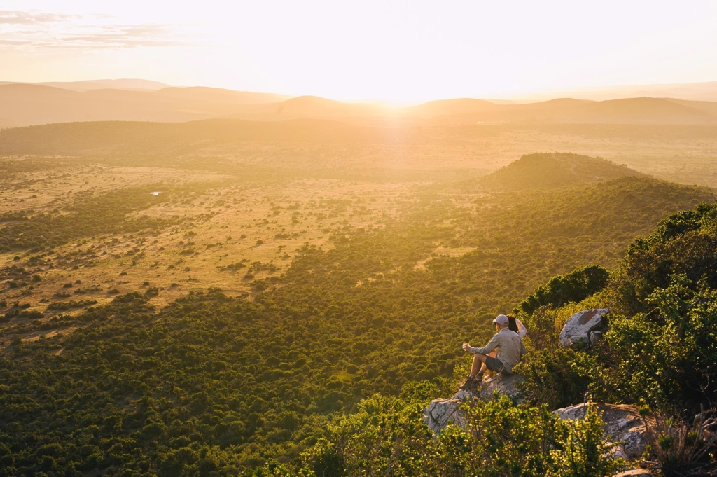 A person sitting on a rock overlooking a vast landscape during sunset.