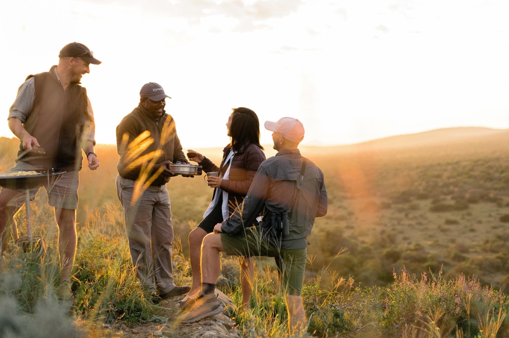 A group of four people enjoying food and drinks outdoors at sunset.