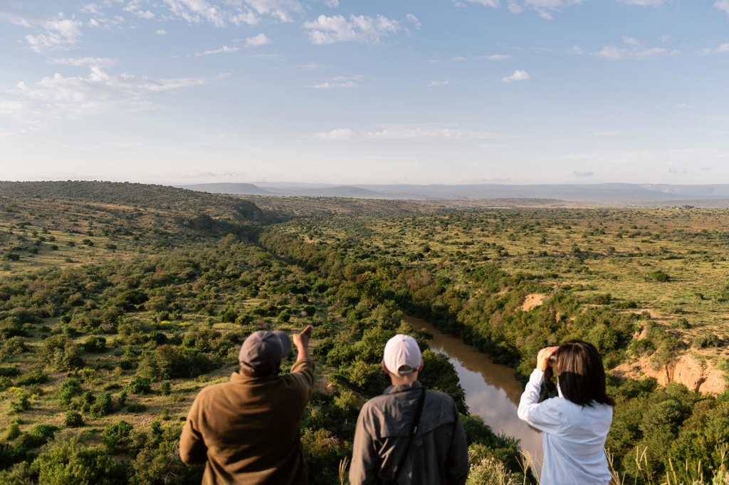 Three people overlooking a valley with a river surrounded by greenery.