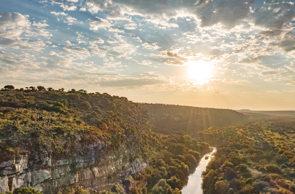 A scenic view of a river winding through a lush landscape under a bright sky at sunset.