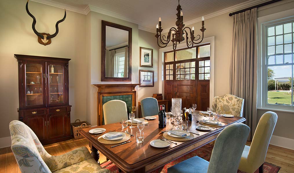A stylish dining room featuring a wooden table set with plates and glasses, surrounded by elegant chairs and decorated with a chandelier and wall mirror.