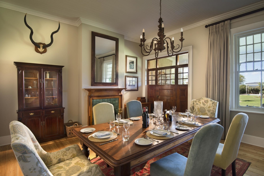 A stylish dining room featuring a wooden table set with plates and glasses, surrounded by chairs and a decorative chandelier.