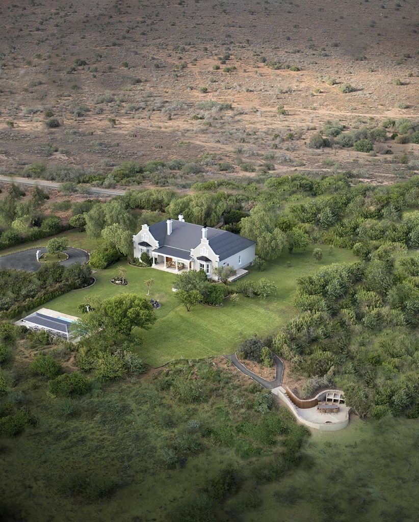 Aerial view of a large white house surrounded by green foliage and open land.