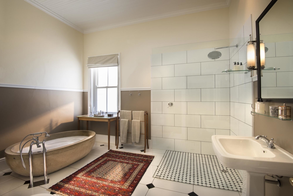 A modern bathroom featuring a freestanding bathtub, shower area, and sink with decorative rugs.