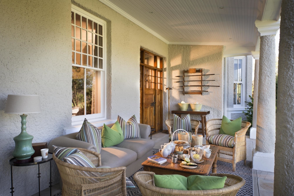 A cozy outdoor seating area with a table set for tea, surrounded by cushions and natural light.